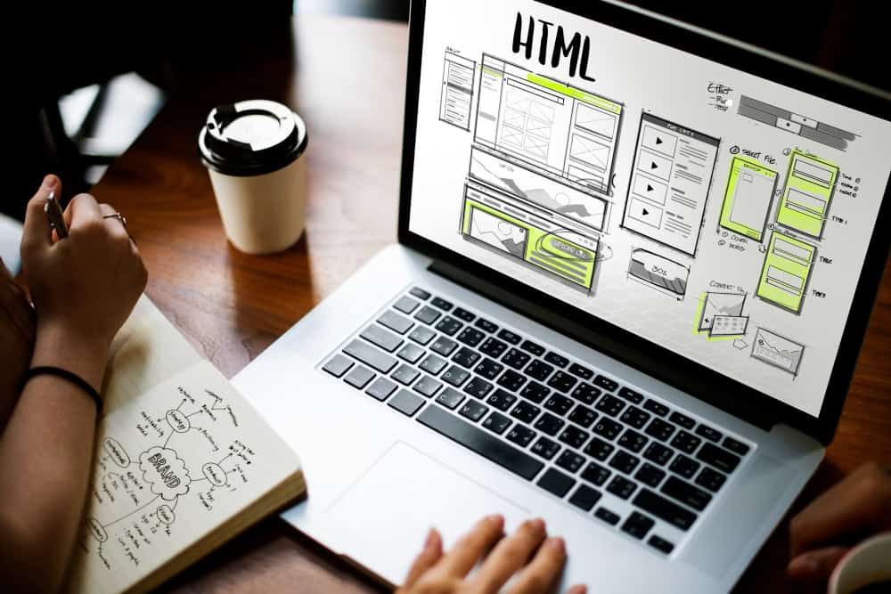 Person working on HTML website design on laptop with sketches and coffee.