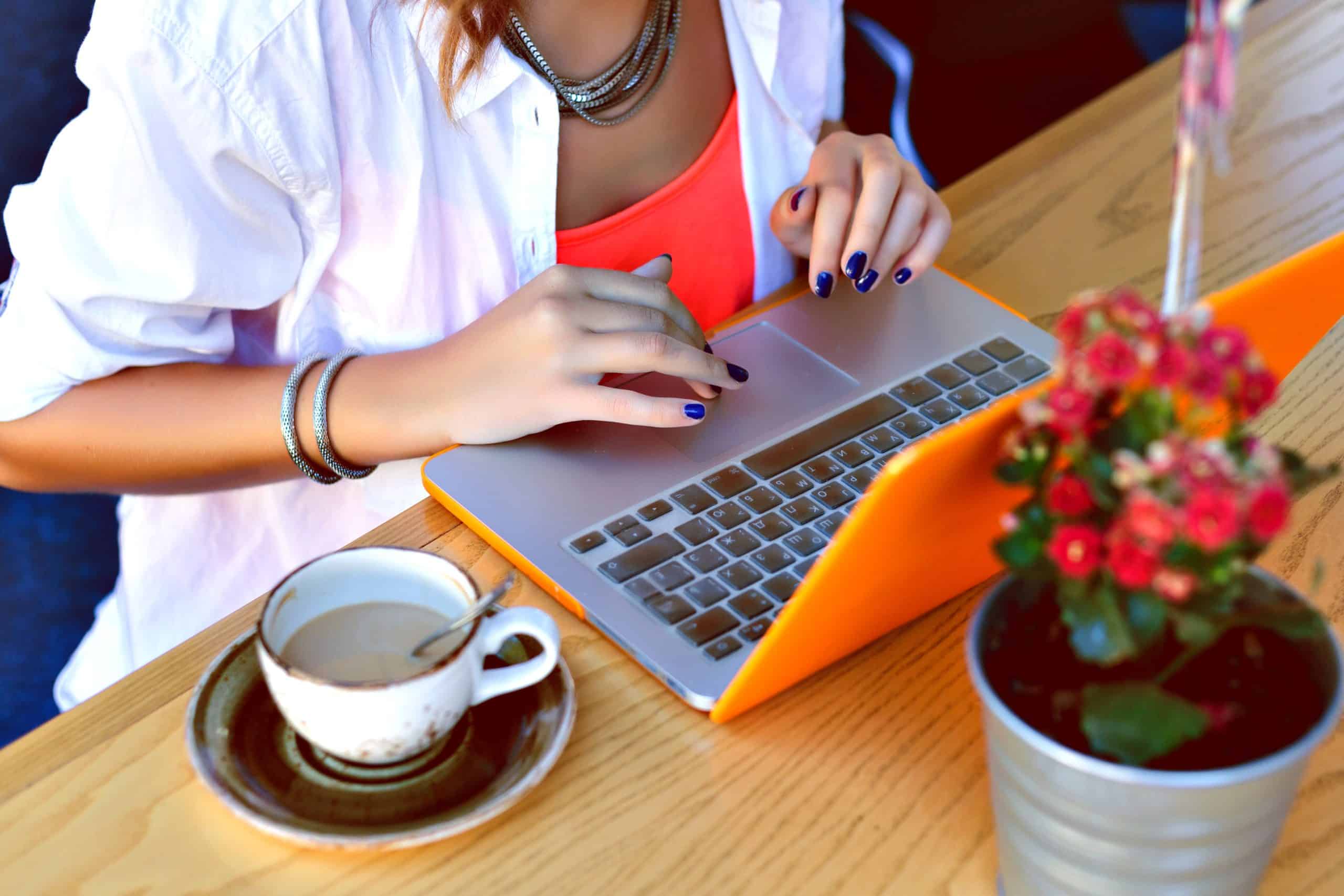 Woman working on laptop with coffee and plant on wooden table.